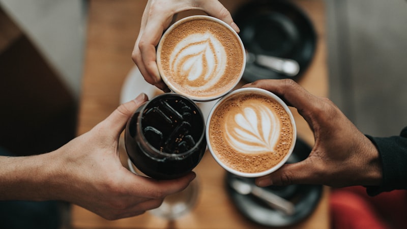 ラテアートのコーヒーカップを3人で乾杯する手元